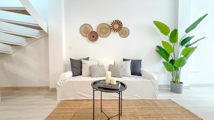 Livingroom Sala luminosa con sofá blanco, cojines grises, planta verde y decoraciones en la pared.