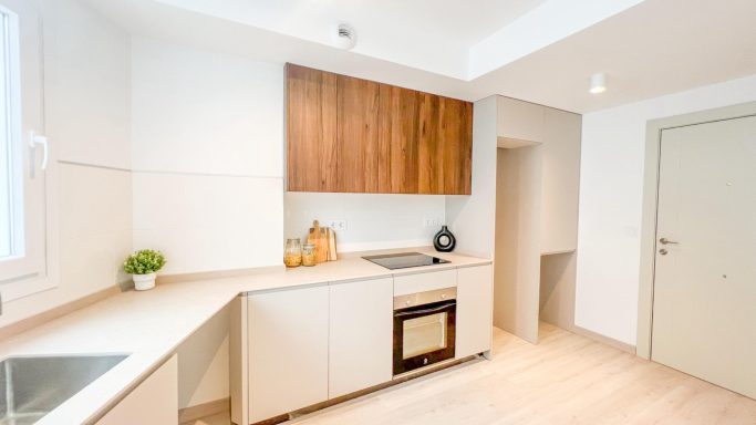 Cocina moderna con muebles claros, encimera de piedra y electrodomésticos integrados.