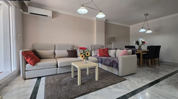 Sala de estar moderna con sofá, mesa de centro y área de comedor con flores.