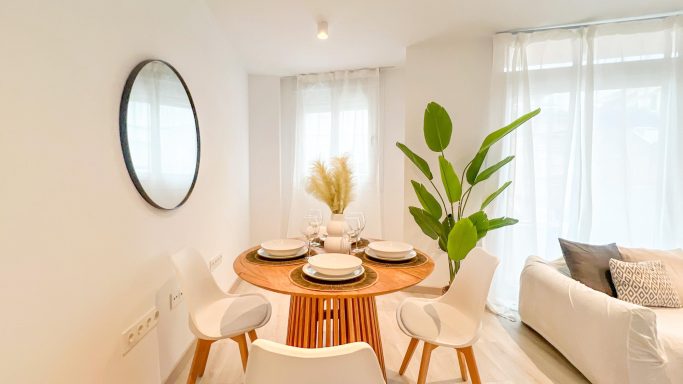 Mesa de comedor redonda con sillas blancas y decoración minimalista en un ambiente luminoso.