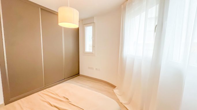 Habitación luminosa con armario y ventana, decorada con cortinas blancas.