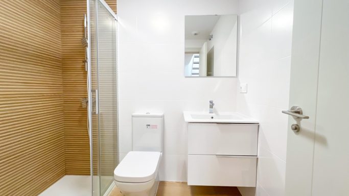 Toilette Baño moderno con ducha, lavabo blanco y pared de madera clara.
