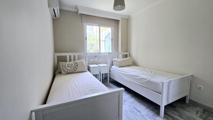 Habitación con dos camas individuales, ventana y decoración minimalista en tonos claros.