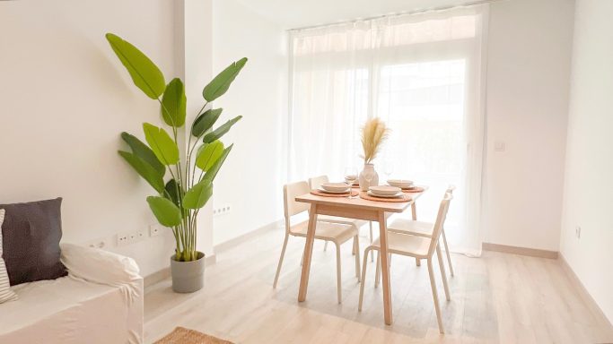 Sala de Estar - Comedor luminoso con mesa de madera, sillas y planta decorativa en una sala minimalista.