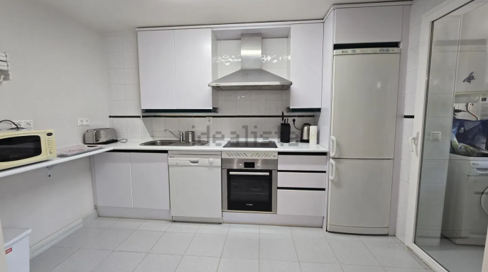 Cocina moderna con electrodomésticos, encimeras blancas y una gran ventana.