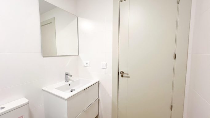 Baño con lavabo moderno, espejo y puerta blanca.