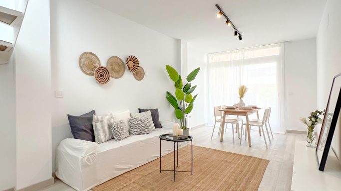 Living Room Salón luminoso con sofá blanco, mesa de centro y planta, decorado con cestas en la pared.