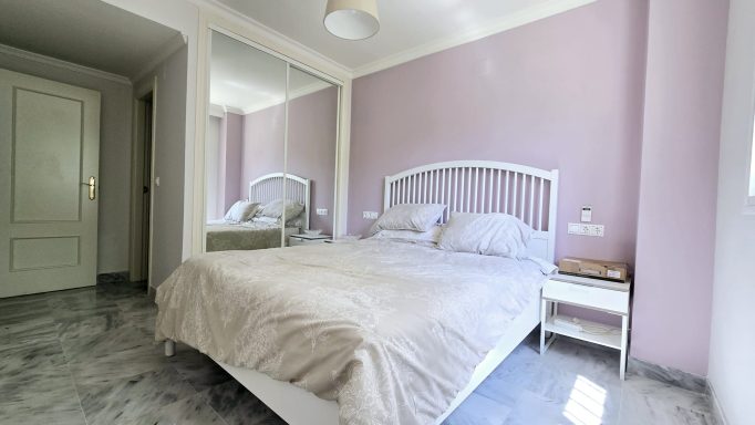 Habitación con cama doble, paredes rosas y decoración minimalista. Suelo de mármol.